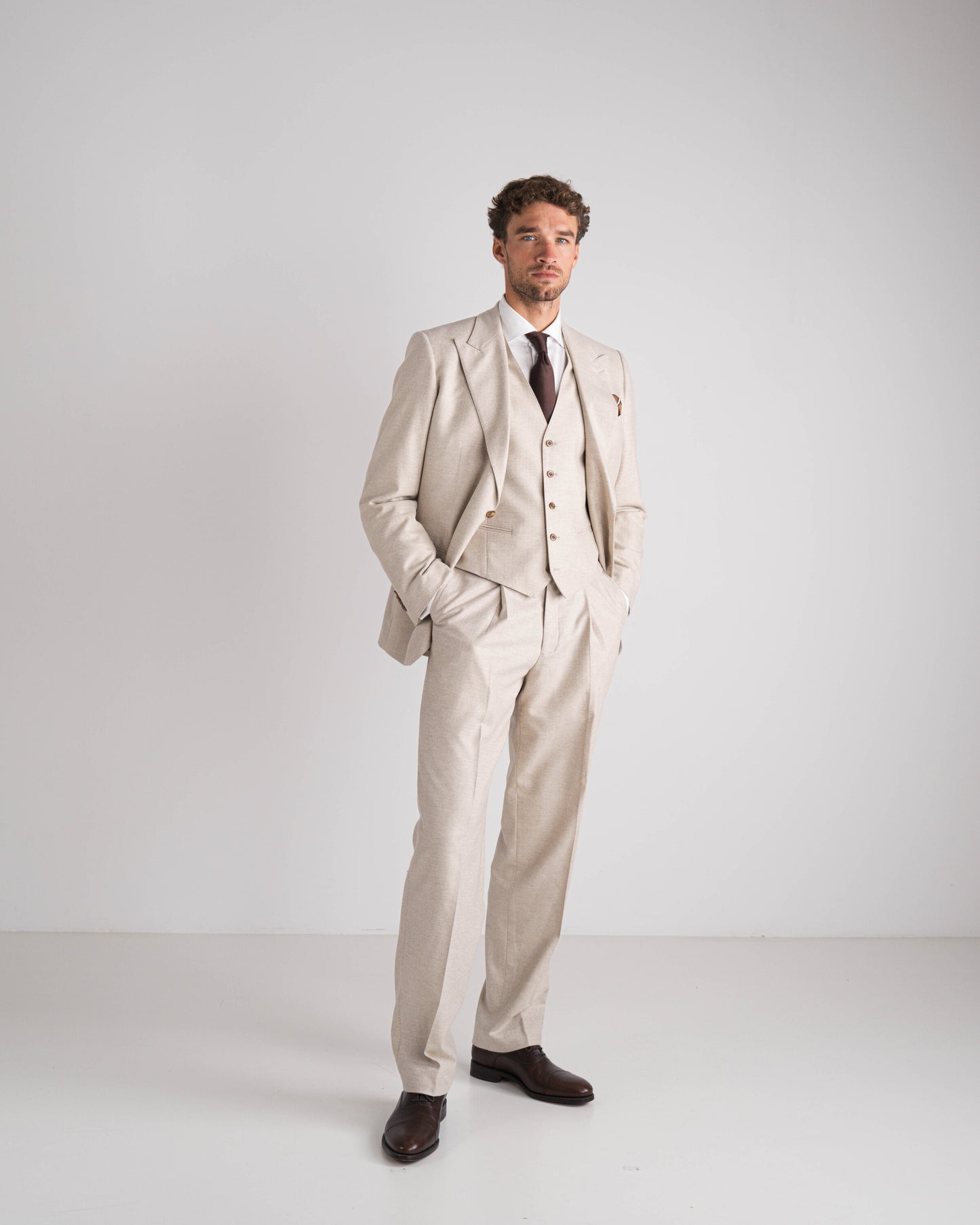 Man in beige drie delig kostuum met bruine das