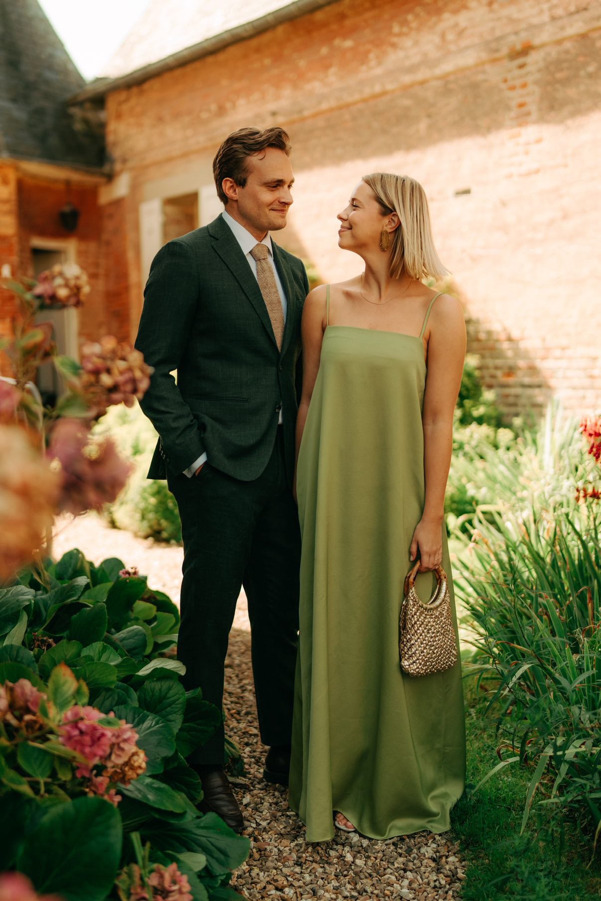 Man in a suit and woman in a green dress standing in a garden.