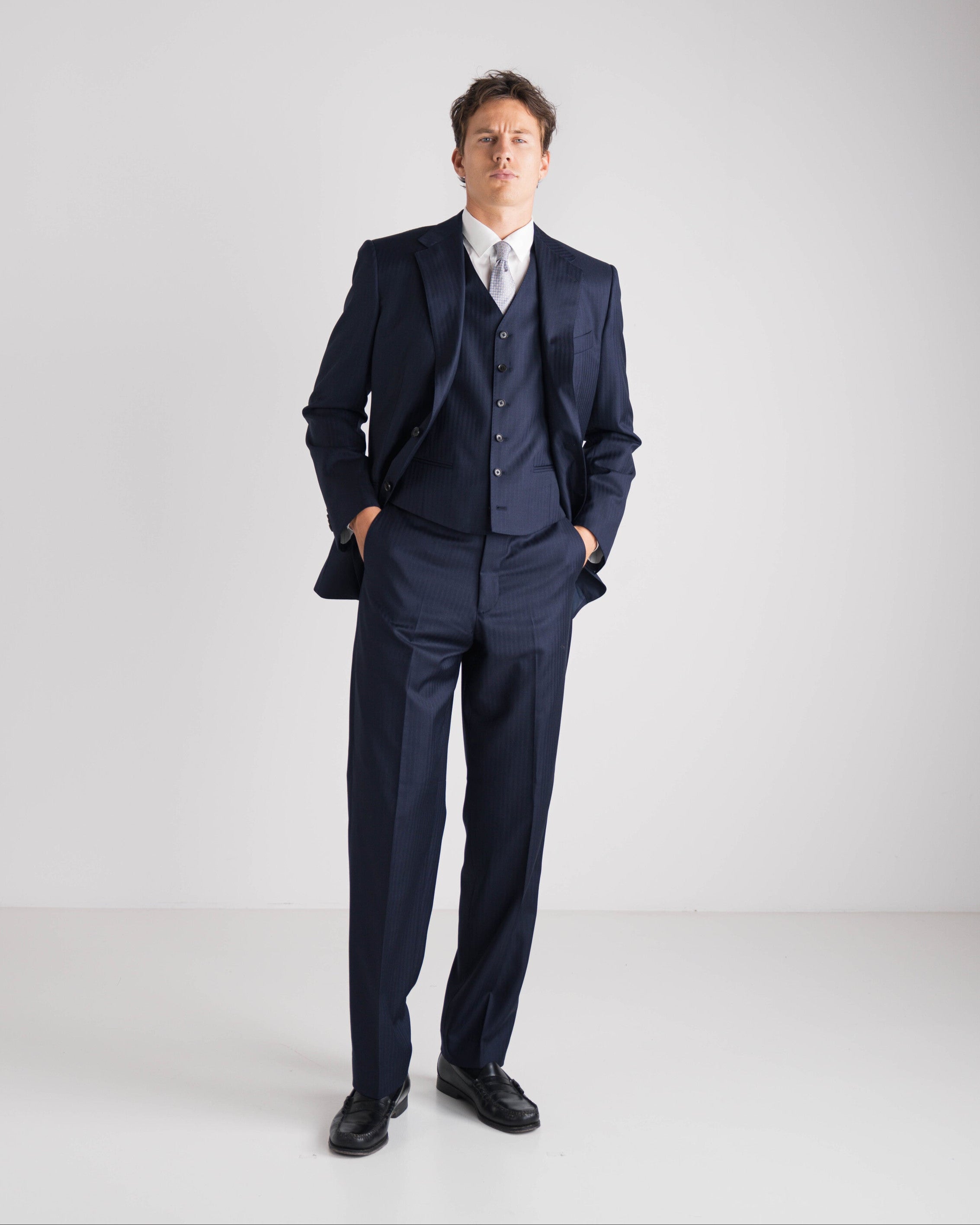 Man wearing a navy blue suit with a white shirt on a light gray background