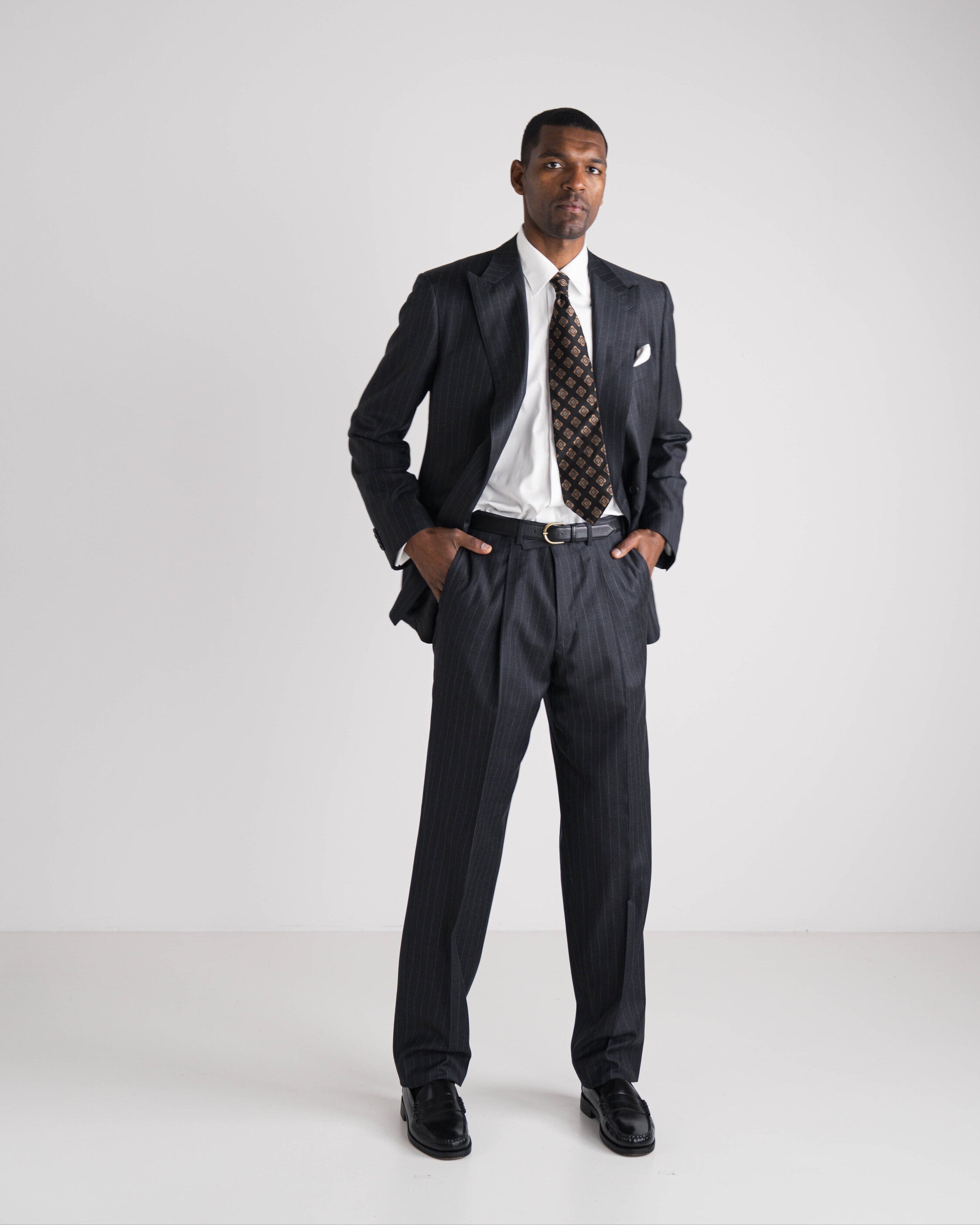 Man wearing a black suit with a white shirt and patterned tie on a white background