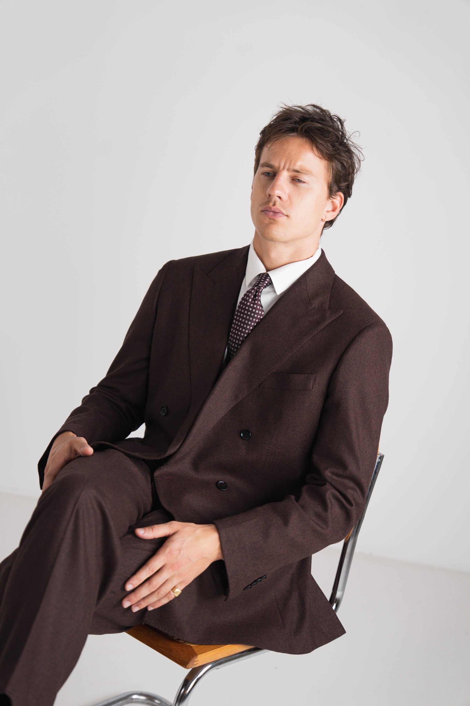 Man wearing a brown suit sitting on a chair against a white background