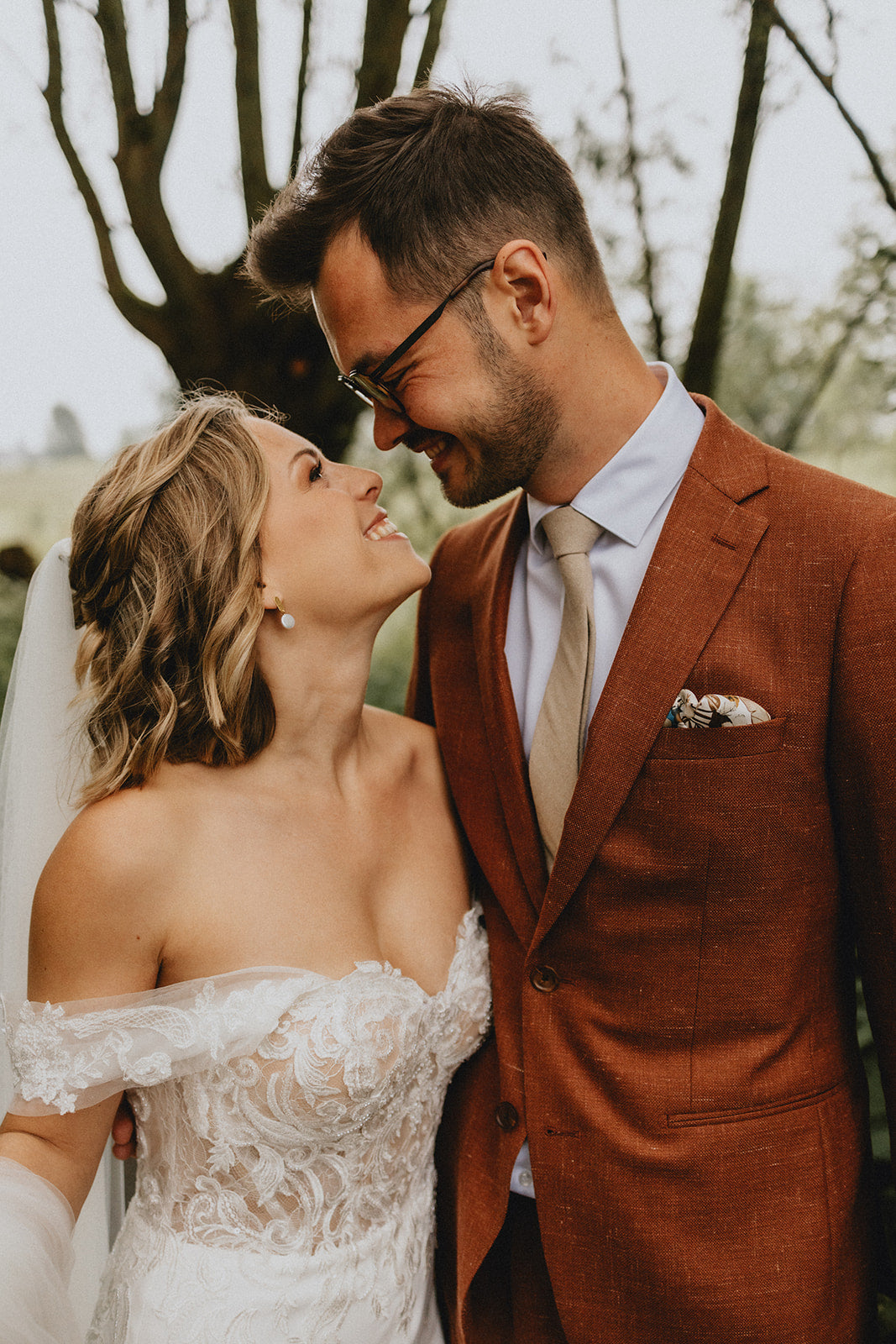 Couple in wedding attire embracing outdoors with trees in the background